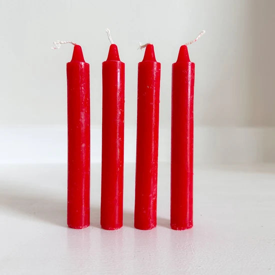 Four red altar candles with white wicks standing upright on a light surface against a plain light background.
