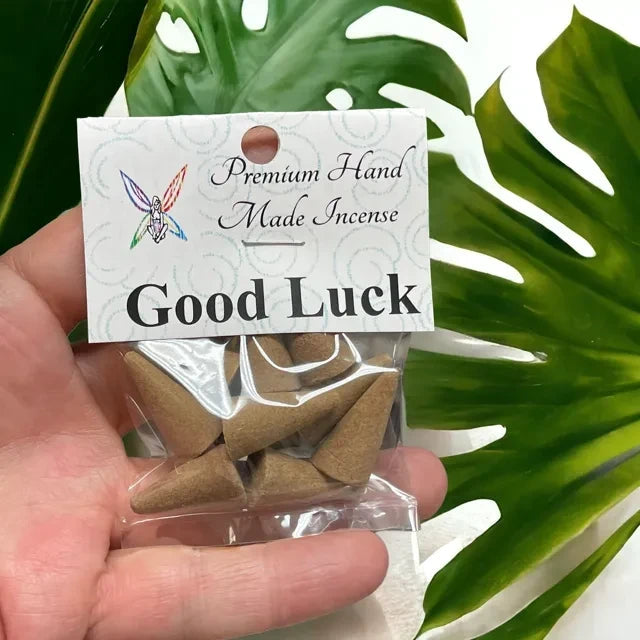 Crystal Fairy Patch Good Luck premium hand-made incense cones in a clear plastic bag held against a monstera leaf background.