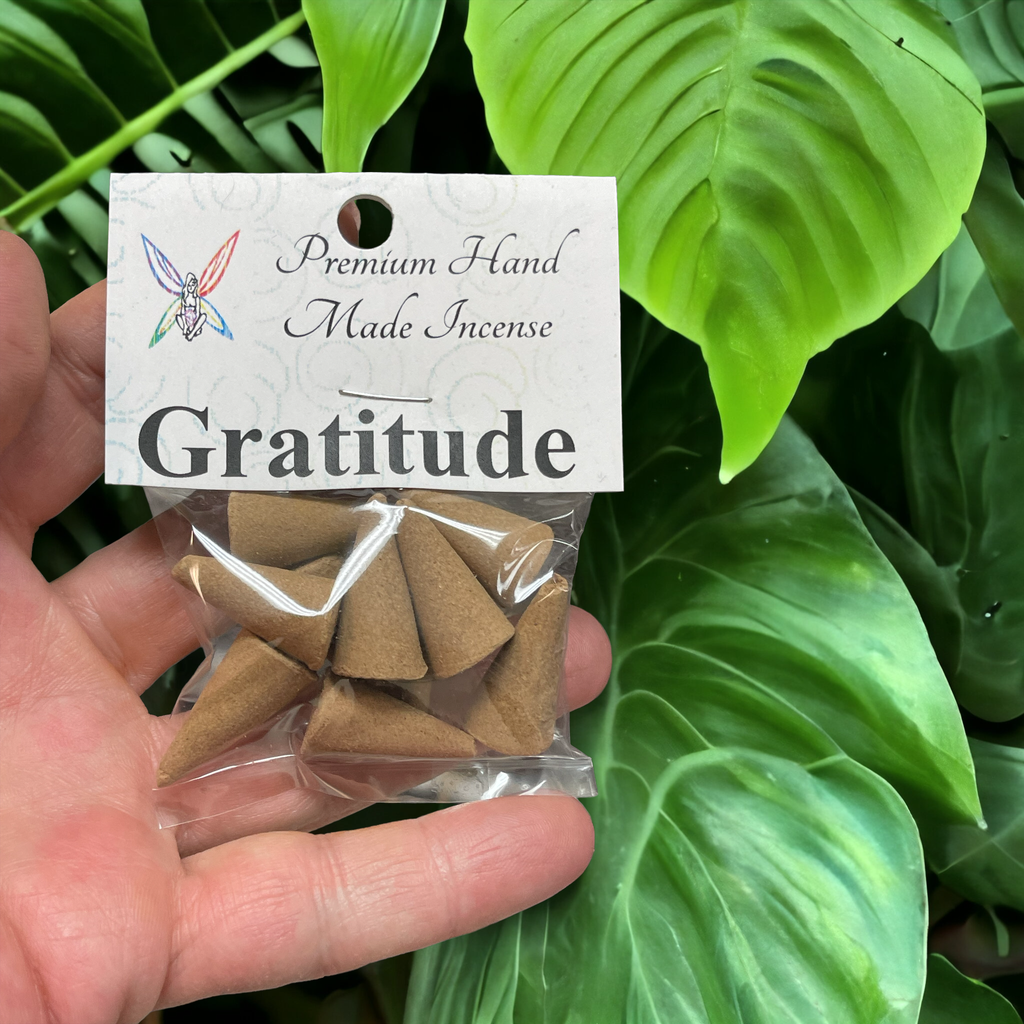 Crystal Fairy Patch Gratitude premium hand-made brown cone incense in a clear plastic bag held against green tropical leaves