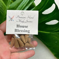 Crystal Fairy Patch House Blessing premium hand-made incense cones in a clear plastic bag held against a green monstera leaf.